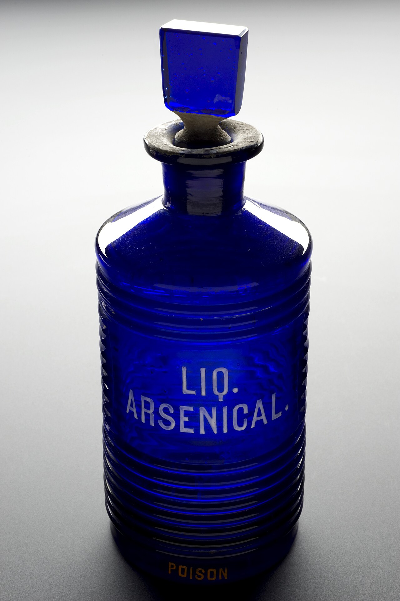 A ridged blue glass poison bottle photographed against black