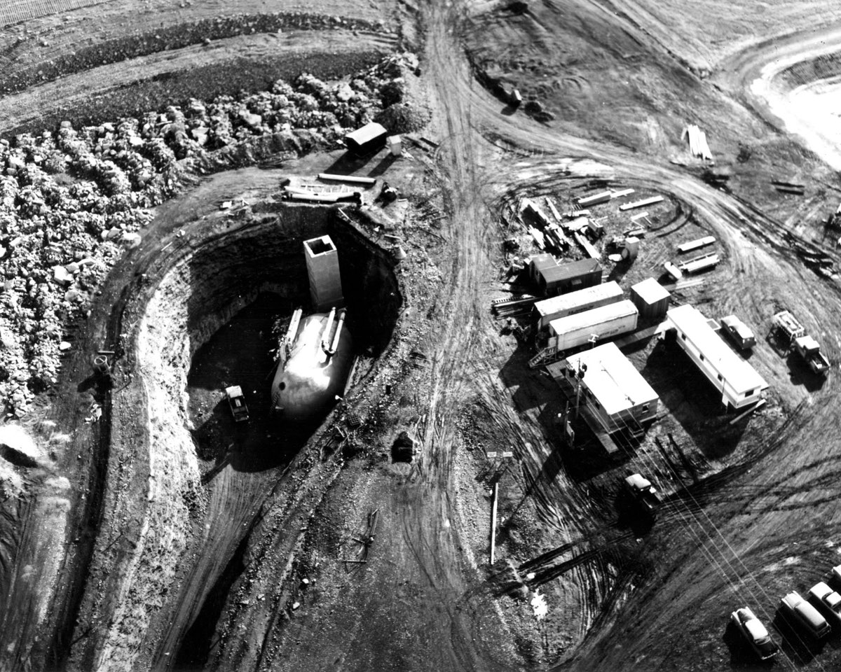 Black-and-white photograph of a Minuteman launch control facility under construction, excavated ground and concrete works in open Montana country.